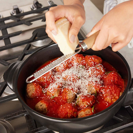 Grated cheese being added to meatballs in tomato sauce using an Xtrema ceramic pot.