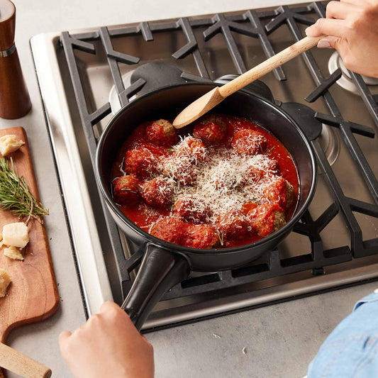 Meatballs in tomato sauce simmering in a black Xtrema ceramic pot on a gas stove.