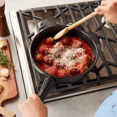 Meatballs in tomato sauce simmering in a black Xtrema ceramic pot on a gas stove.