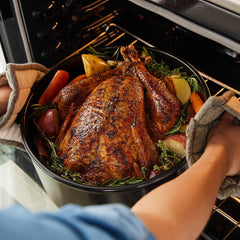 A roasted turkey with vegetables in a black Xtrema ceramic roasting pan being removed from an oven.