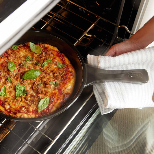 A cooked pizza in an Xtrema ceramic skillet being removed from an oven with a towel.