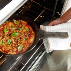 A cooked pizza in an Xtrema ceramic skillet being removed from an oven with a towel.