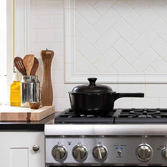 Black Xtrema ceramic pot with lid on a stainless steel gas stovetop in a white kitchen.