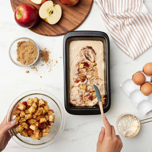 Apple cake batter in a black Xtrema ceramic loaf pan with cinnamon apples and brown sugar.