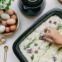 Hand garnishing fresh dough with herbs and flowers in an Xtrema ceramic baking pan.