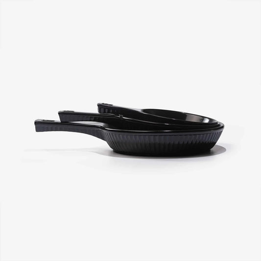 Three stacked black Xtrema pure ceramic cookware pans with handles on a white background.