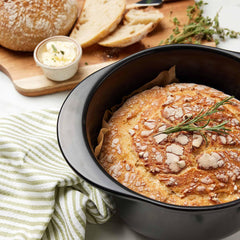 Freshly baked sourdough bread in a black Xtrema ceramic baking dish with rosemary garnish.