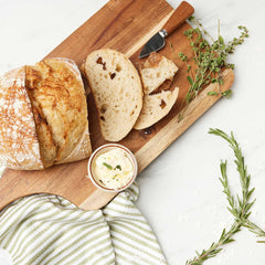 Freshly baked sourdough bread with butter and herbs on a wooden board.