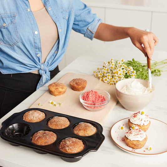 Person frosting homemade muffins using Xtrema ceramic bakeware on a white countertop.