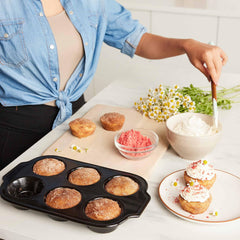Person frosting homemade muffins using Xtrema ceramic bakeware on a white countertop.