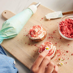 Hand decorating red velvet cupcakes on a wooden board with Xtrema baking tools.