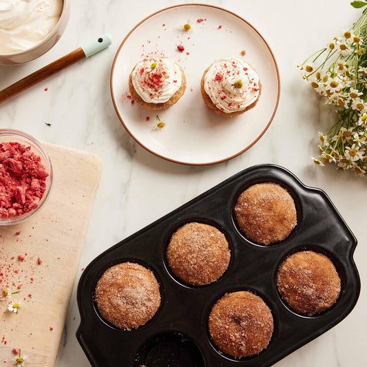 Freshly baked muffins in a black Xtrema baking pan alongside frosted cupcakes.