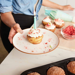 A person holding a white Xtrema ceramic plate with a single lit birthday cupcake.