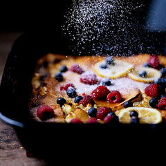 Fresh berries and lemon slices on a dessert in an Xtrema ceramic baking dish, dusted with sugar.