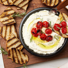 Roasted tomatoes and olive oil on creamy dip in a black Xtrema ceramic bowl with grilled toast.