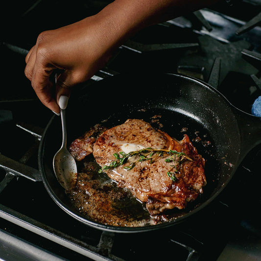 Searing a steak with butter and thyme in an Xtrema ceramic skillet on a gas stove.