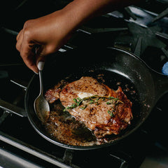 Searing a steak with butter and thyme in an Xtrema ceramic skillet on a gas stove.