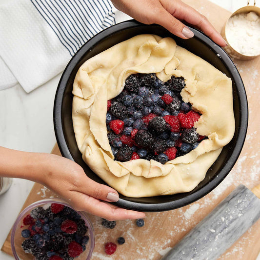 A berry pie with a pastry crust being prepared in a black Xtrema ceramic pie dish.