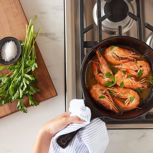 Shrimp sautéing in a black Xtrema ceramic pan on a gas stove with fresh parsley.