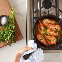 Shrimp sautéing in a black Xtrema ceramic pan on a gas stove with fresh parsley.