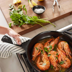 Shrimp simmering in a black Xtrema ceramic pan with fresh herbs on a stovetop.