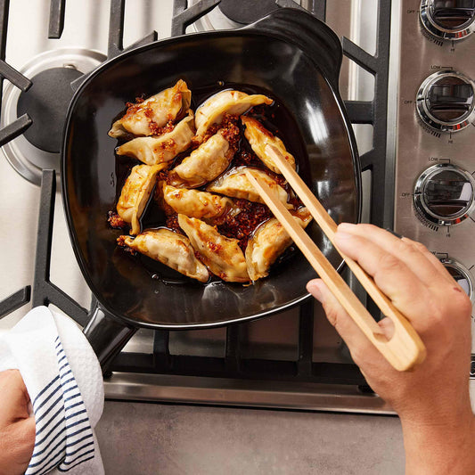 Dumplings cooking in an Xtrema ceramic skillet with chili oil and chopsticks.