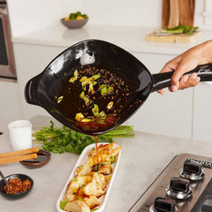 Person pouring stir-fry from an Xtrema ceramic wok onto a platter of dumplings.