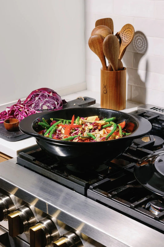Fresh vegetable stir-fry cooking in a black Xtrema ceramic wok on a professional gas stove.