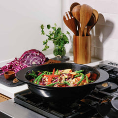 Xtrema pure ceramic wok on a gas stove filled with colorful stir-fry vegetables.