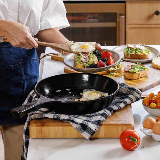 A person using a wooden spatula to plate a fried egg from an Xtrema ceramic skillet.