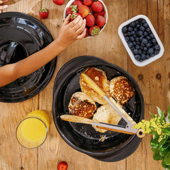 Pancakes cooking in a black Xtrema ceramic pan with fresh strawberries and blueberries.