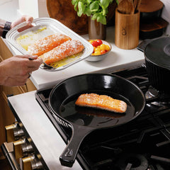 Salmon fillets searing in a black Xtrema ceramic skillet on a gas stove.