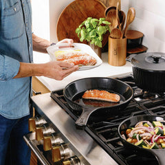 A person preparing salmon in Xtrema ceramic cookware on a professional kitchen range.