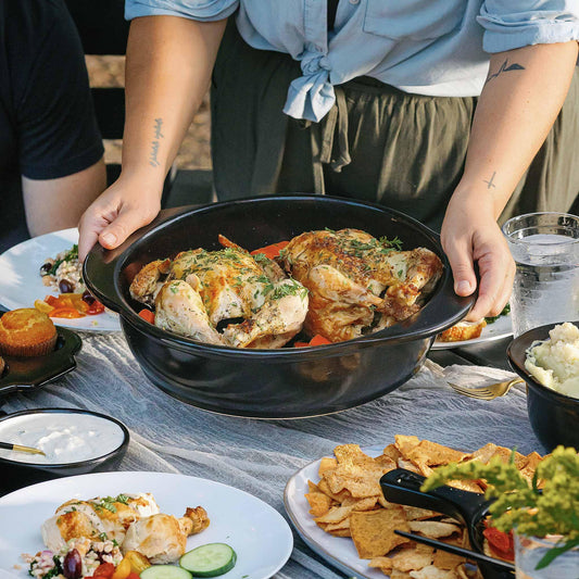 Whole roasted chickens served in a black Xtrema ceramic roasting pan on a dinner table.