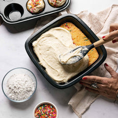 Spreading white frosting on a cake in a black Xtrema ceramic baking pan.