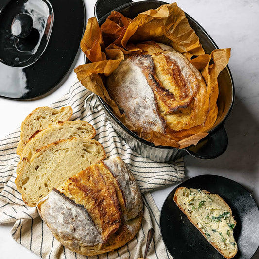 Freshly baked sourdough bread in a black Xtrema ceramic pot with sliced pieces on a linen cloth.