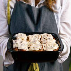 Person holding a black Xtrema ceramic baking dish filled with frosted cinnamon rolls.