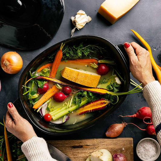 Hands holding an Xtrema ceramic pan filled with a colorful vegetable soup and tofu.