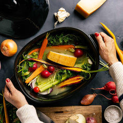 Hands holding an Xtrema ceramic pan filled with a colorful vegetable soup and tofu.