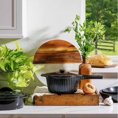 Black Xtrema ceramic pot with lid on a rustic wooden tray in a bright kitchen setting.