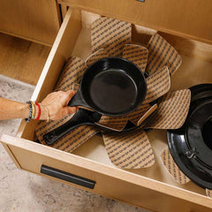 A hand organizing black Xtrema ceramic cookware in a drawer with protective liners.