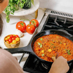 A black Xtrema ceramic skillet cooking tomato sauce on a gas stove with fresh vegetables.