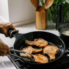 Pork chops searing in a black Xtrema ceramic skillet on a gas stovetop.