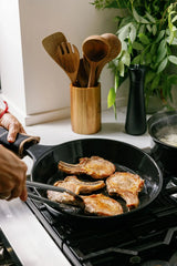 Pork chops searing in a black Xtrema ceramic skillet on a gas stove.
