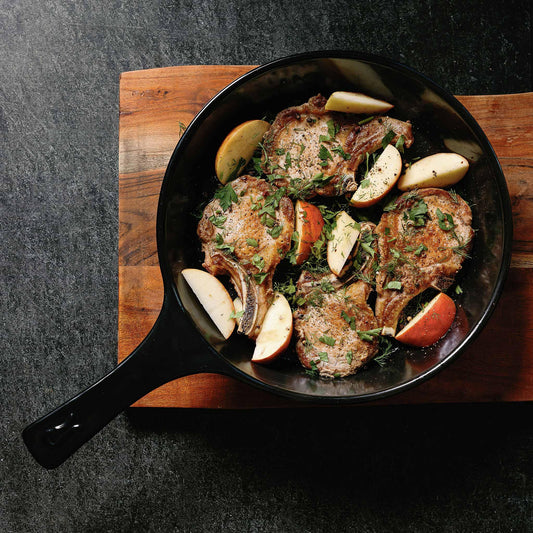 Pan-seared pork chops with apples and herbs in an Xtrema ceramic skillet on a wooden board.