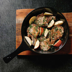 Pan-seared pork chops with apples and herbs in an Xtrema ceramic skillet on a wooden board.