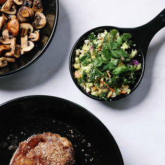 Seared steak, sautéed mushrooms, and a fresh kale salad served in black Xtrema ceramic cookware.