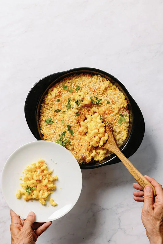 Baked macaroni and cheese in a black Xtrema ceramic pan with a serving on a white plate.