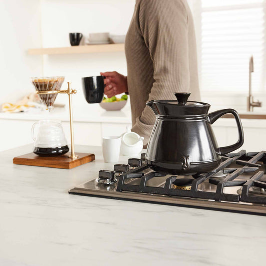 Xtrema black ceramic teapot on a modern gas stovetop in a bright kitchen setting.