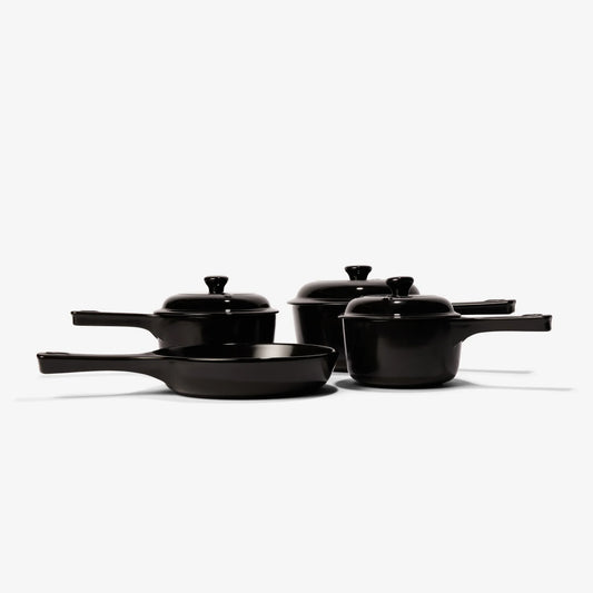 Set of black Xtrema pure ceramic cookware including pans and lidded pots on a white background.